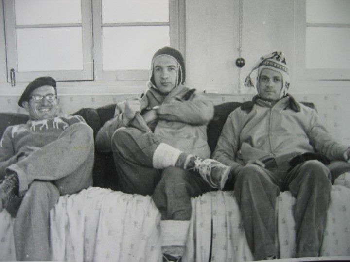 Tres hombres con ropa de montaña sentados en un sofá dentro del refugio.
