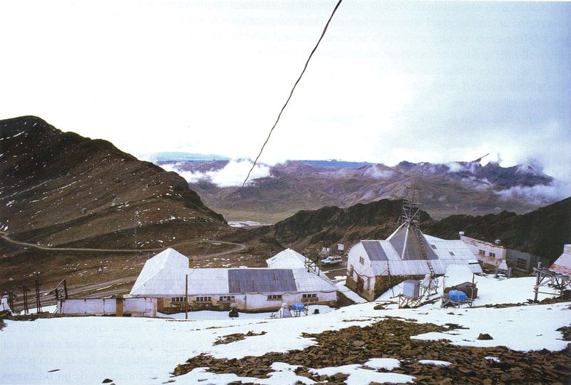 Vista general del Laboratorio de Física Cósmica de Chacaltaya: edificios blancos y una torre metálica sobre la ladera nevada, con la cordillera al fondo.