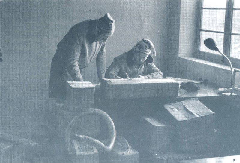 Dos hombres inclinados sobre una mesa de trabajo junto a una ventana.