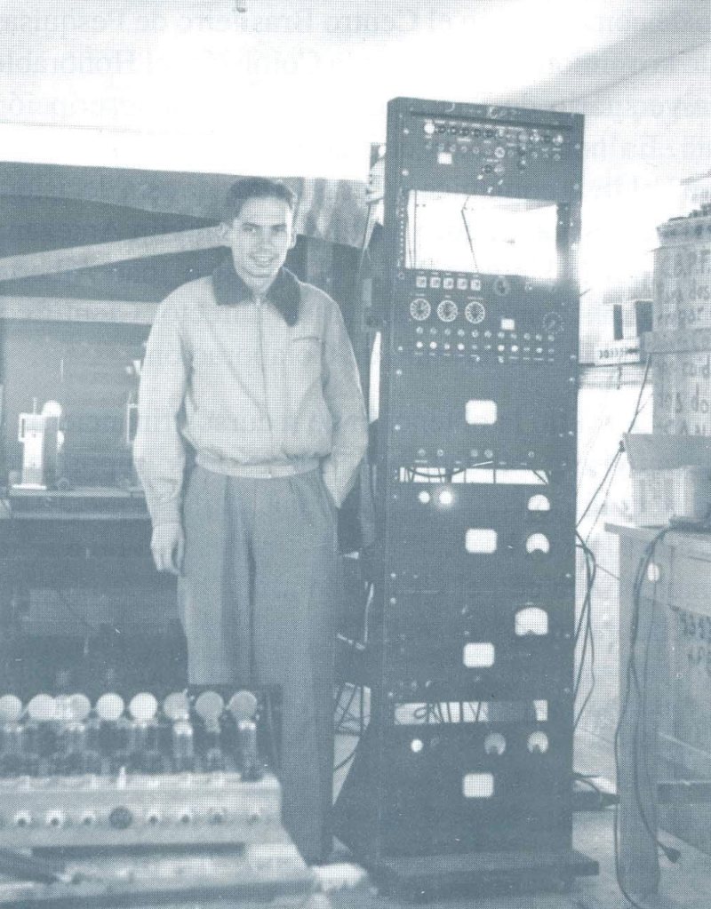 Un hombre de pie junto a un bastidor de válvulas electrónicas.